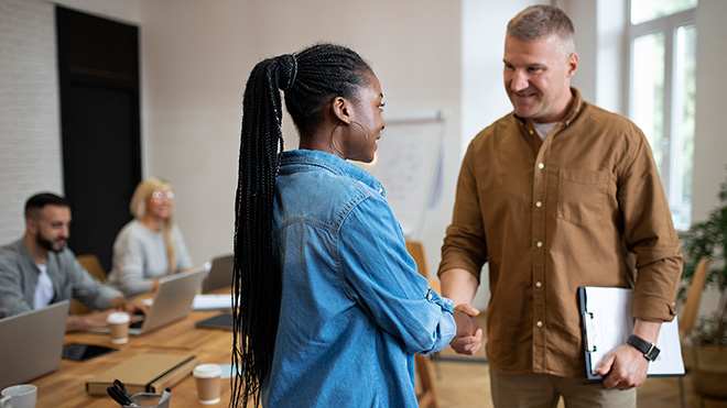 2 people in a board room shacking hands with a contract in one persons hands