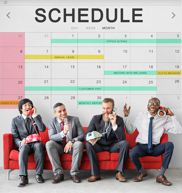 Schedule calendar on large wall, with people on a sofa talking on phones.